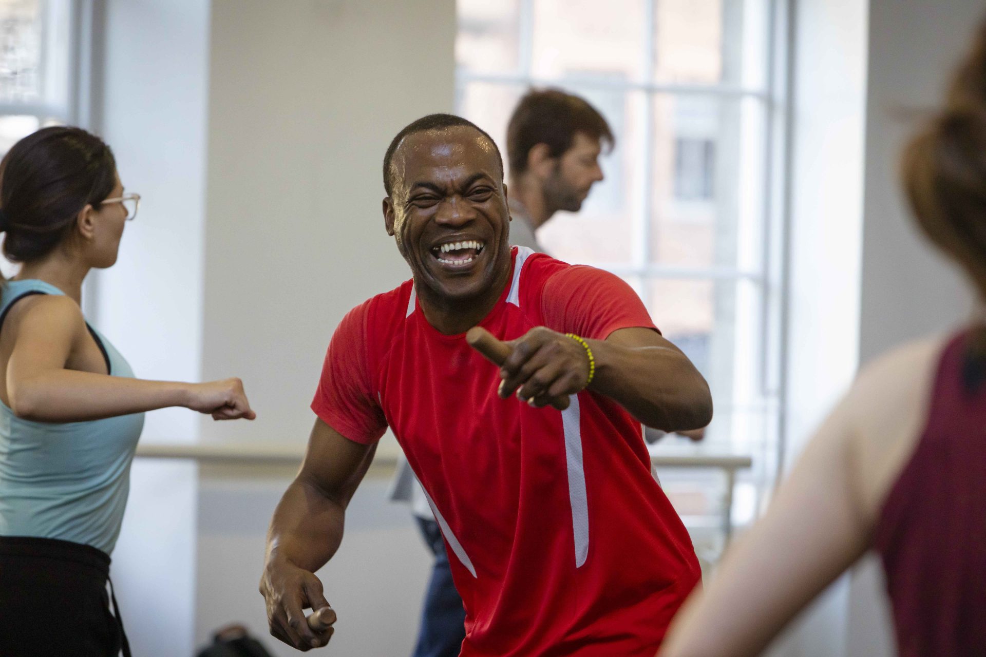 A smiling man in a bright red t-shirt points towards the camera.