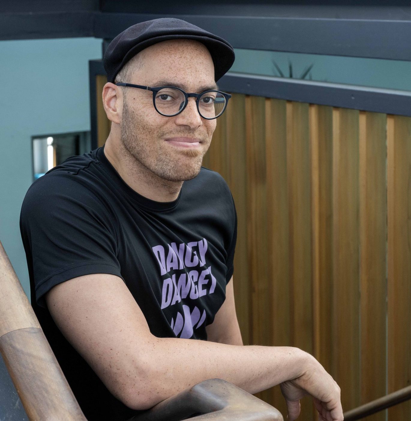 Dance Base's Artistic Director Tony Mills stands in Dance Base's stairwell, wearing a black flat-cap and a t-shirt with the words: 