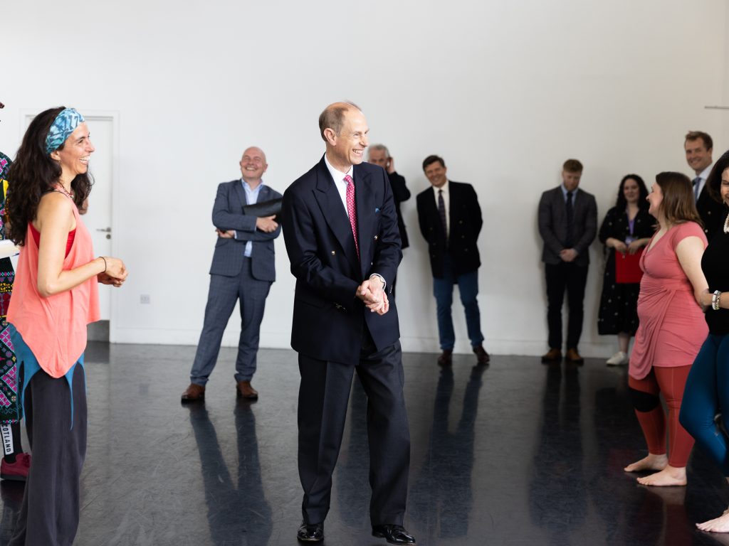His Royal Highness The Duke of Edinburgh stands in a dance studio surrounded by smiling dancers
