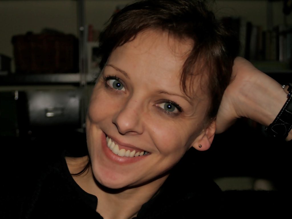 Kally Lloyd-Jones headshot 1.docx A close-up head shot of Kally Lloyd-Jones, smiling a the camera with her hand resting on the back of her head.