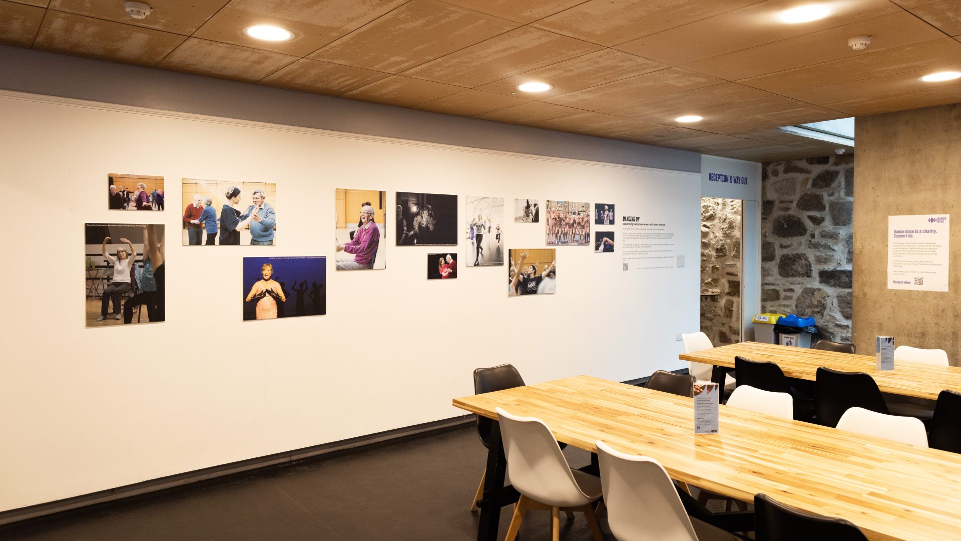 Dancing On Exhibition, Dance Base 2024-25. Image credit Stuart Armitt A view of the exhibition hanging in Dance Base's upper foyer, taken to show the space including tables and chairs.