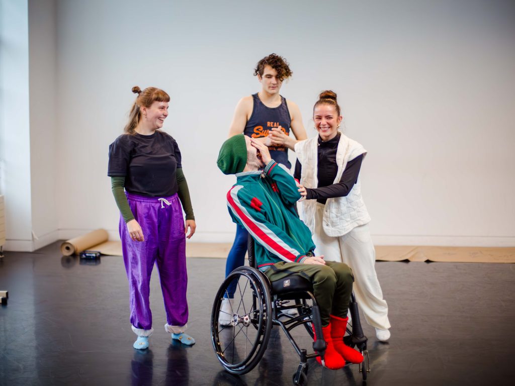 DEBS autumn residency 2025. Image credit: Paul Andrews Three young dancers laugh with their mentor in a brightly lit studio.