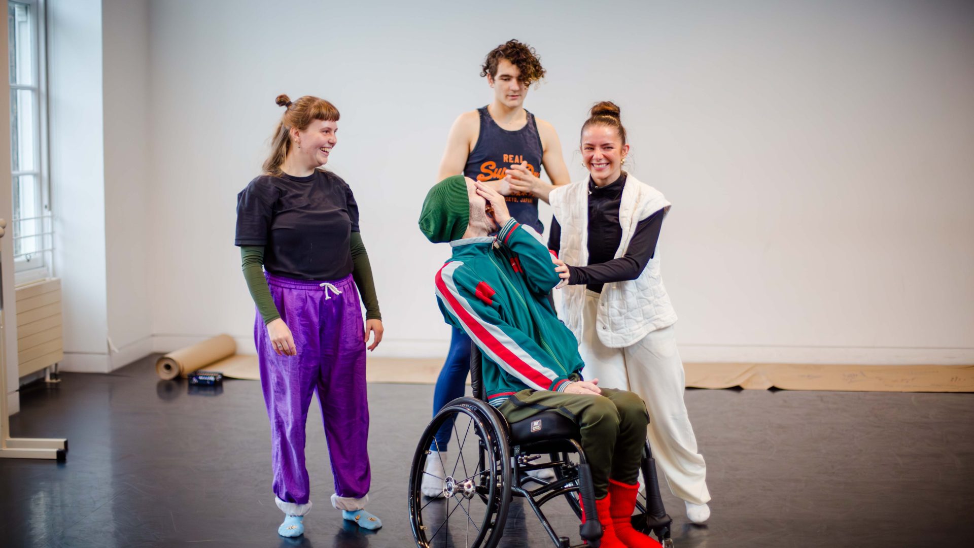 DEBS autumn residency 2025. Image credit: Paul Andrews Three young dancers laugh with their mentor in a brightly lit studio.