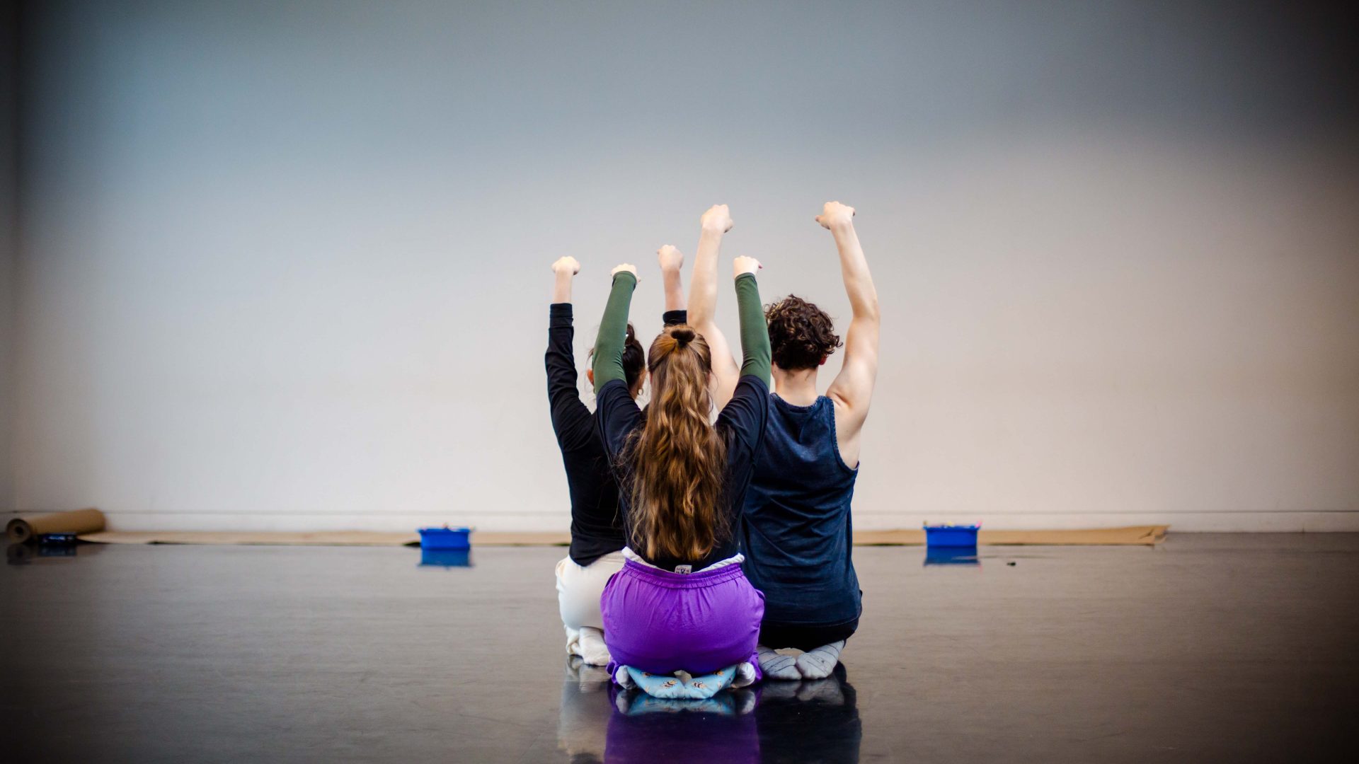DEBS autumn residency 2025. Image credit: Paul Andrews-246 Three young dancers with their backs to the camera kneel on the floor with their arms above their heads.