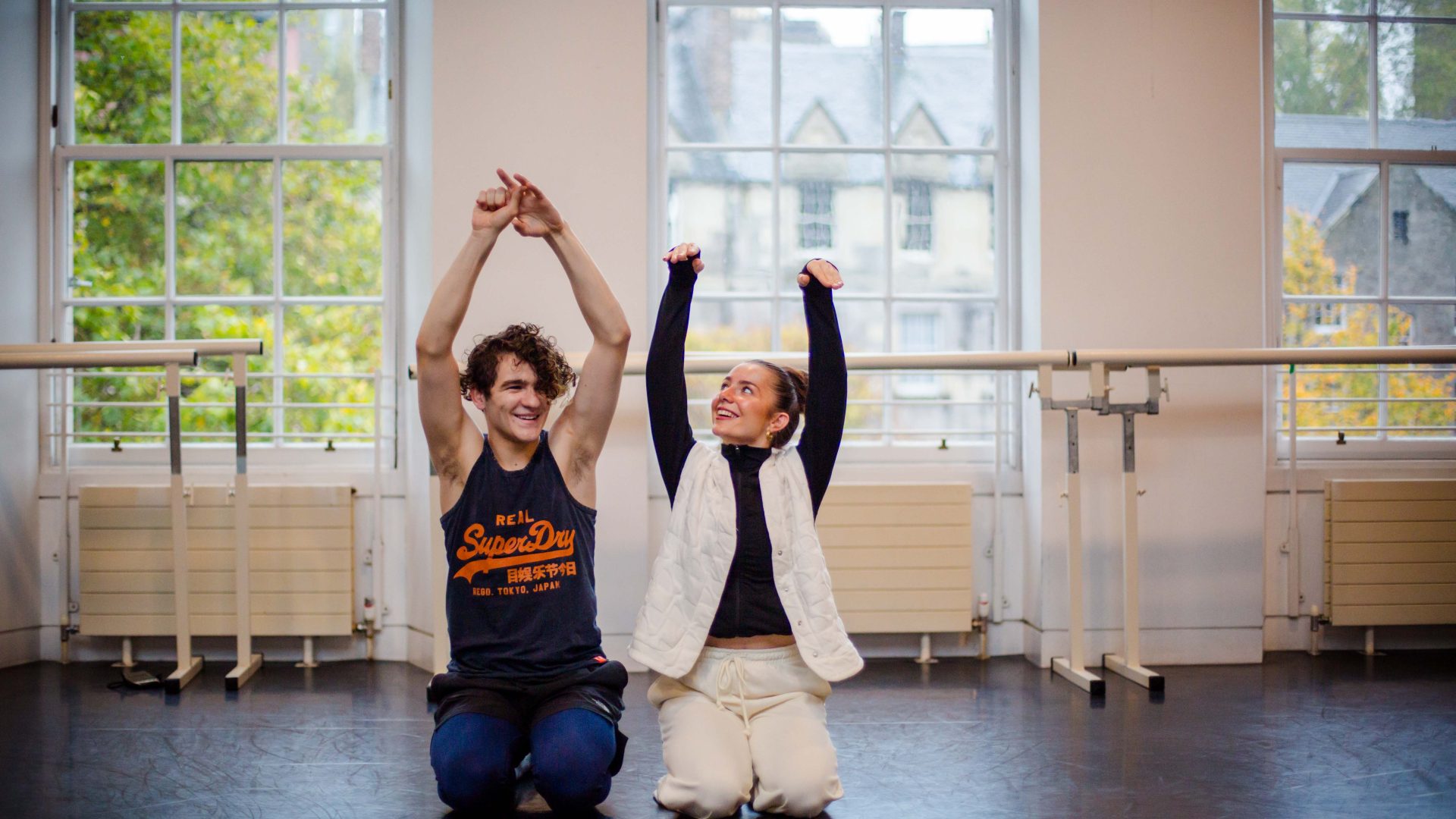 DEBS autumn residency 2025. Image credit: Paul Andrews A dancer using a wheelchair smiles as he dances across a brightly lit studio, with two young dancers behind him.